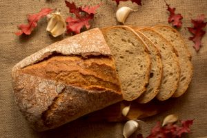 Pokorojony świeży chleb w kompozycji z jesiennymi liśćmi i czosnkiem.
